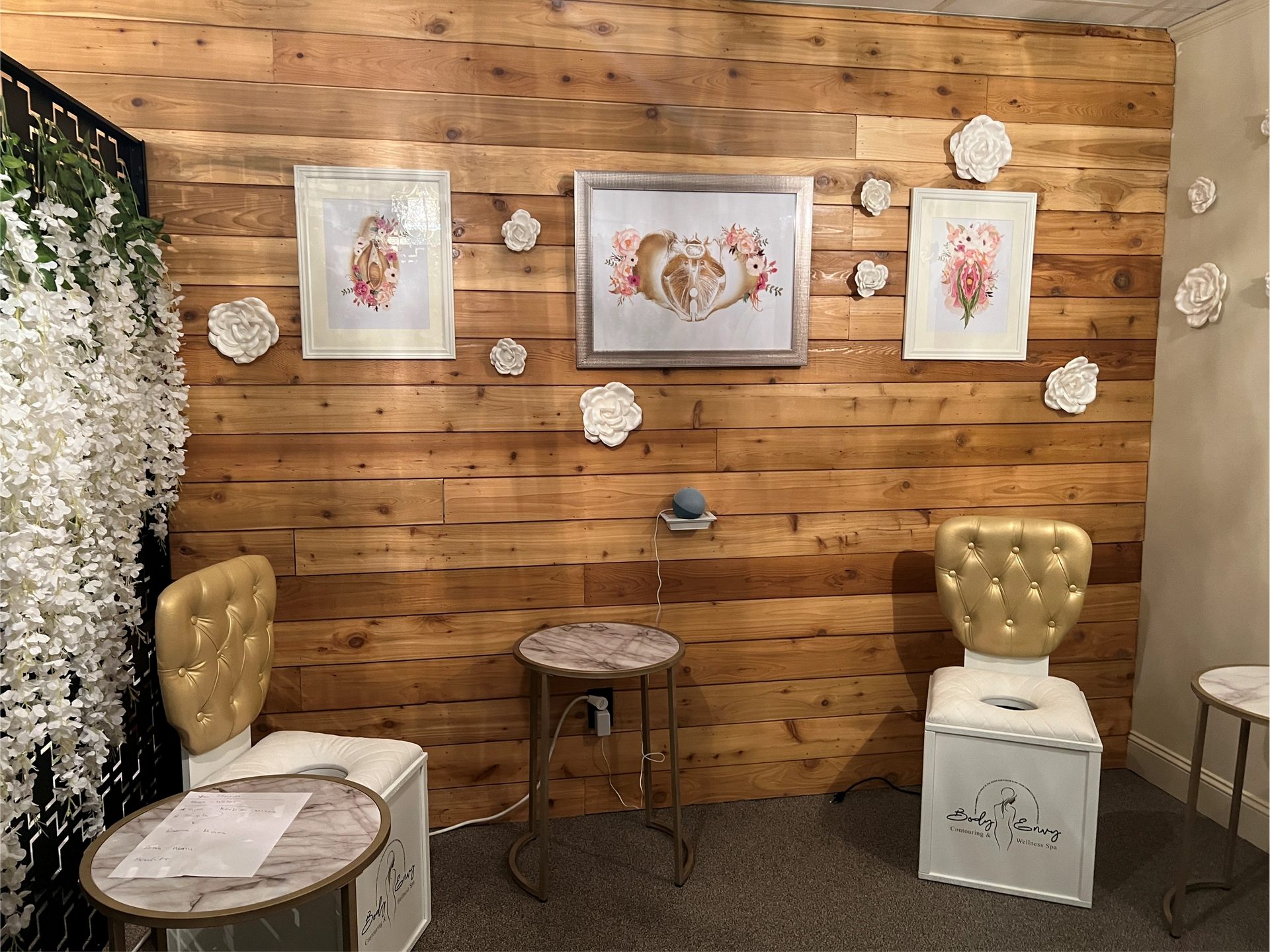 A room with a wood-paneled wall, artwork, chairs, and small tables.