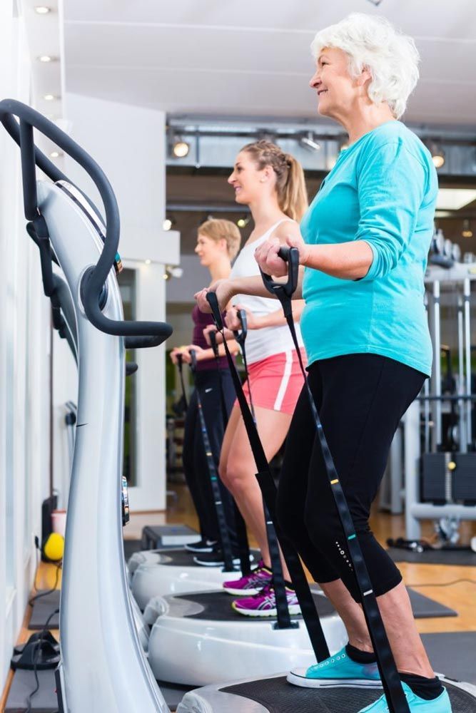 Three women exercising on vibration platforms in a gym, smiling.