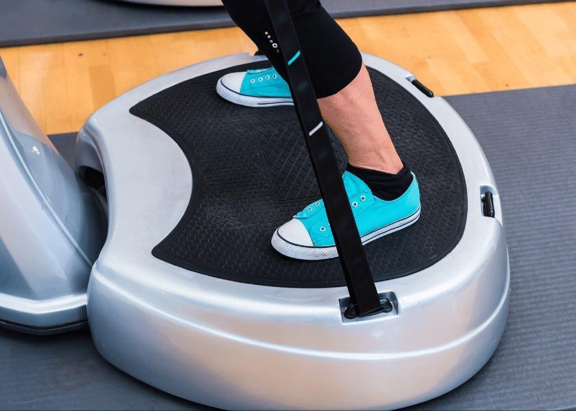 Person on a vibrating exercise platform, wearing teal sneakers. Black support straps.