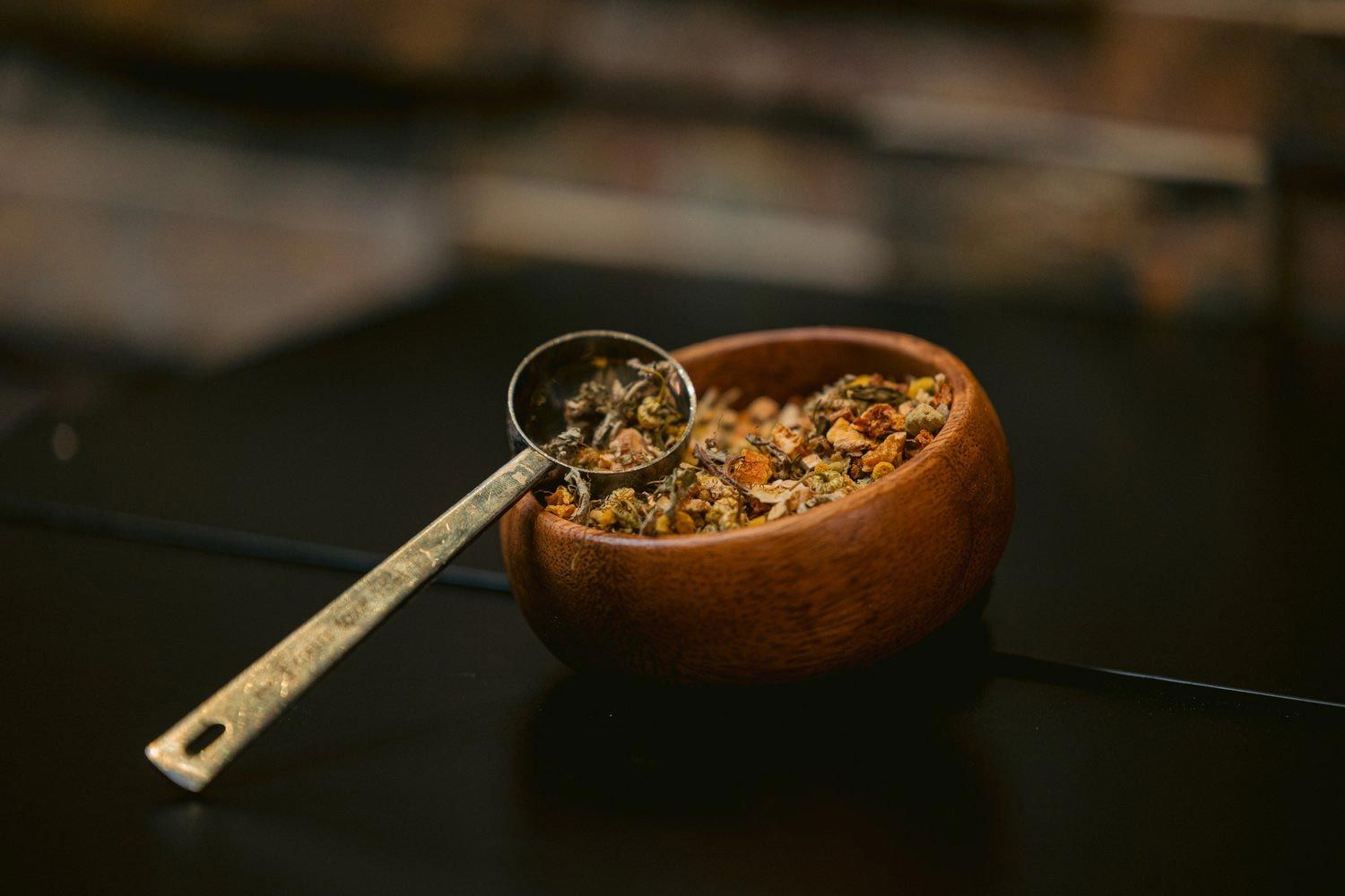 Wooden bowl filled with granola and a golden spoon on a dark surface.
