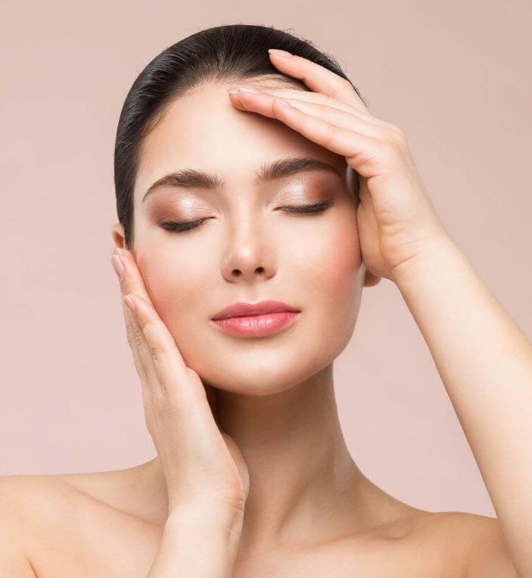 Woman with closed eyes, hands on face, light makeup, against a beige background.