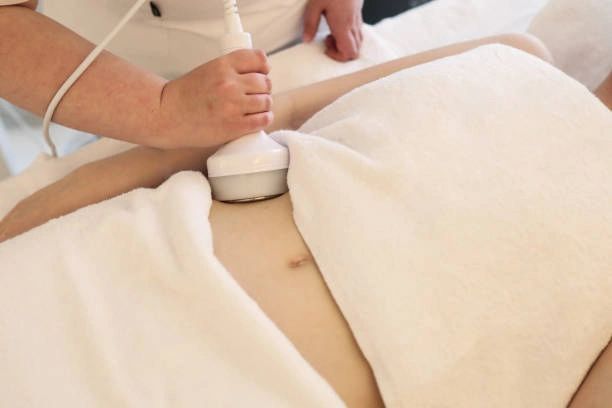 Person receiving body treatment with a handheld device on abdomen, in a spa setting.