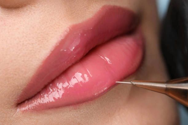 Lip tattoo procedure: needle near glossy pink lips.