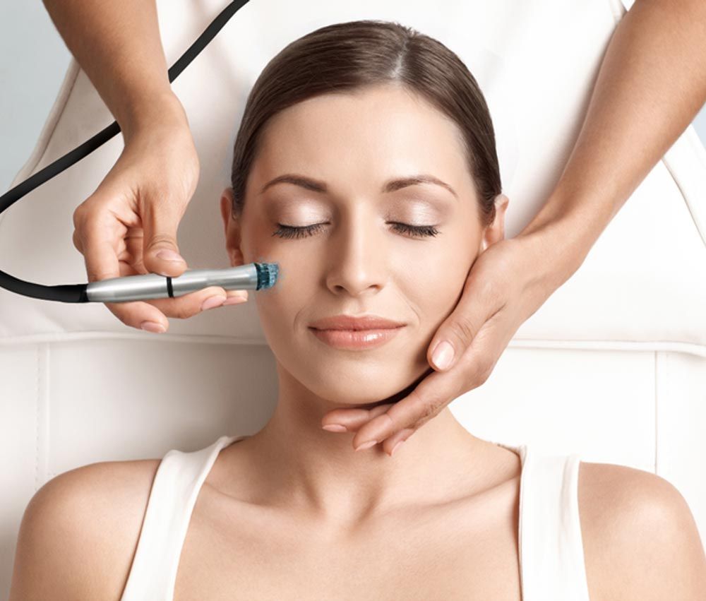 Woman receiving facial treatment; technician holds tool near face, hands on cheeks.