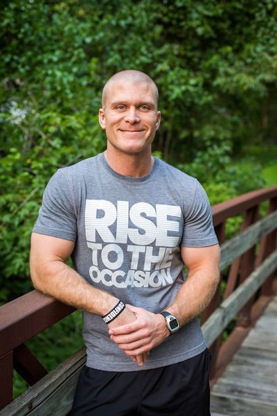 A man wearing a rise to the occasion t-shirt is standing on a bridge.