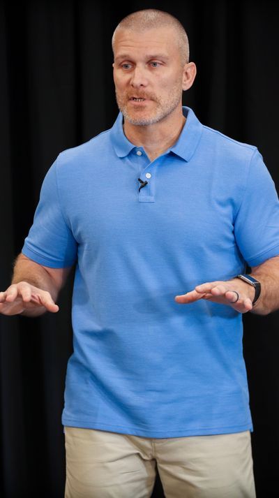 A man in a blue polo shirt is standing in front of a black curtain.