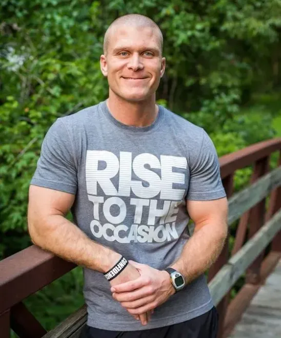 A man wearing a rise to the occasion t-shirt is standing on a bridge.