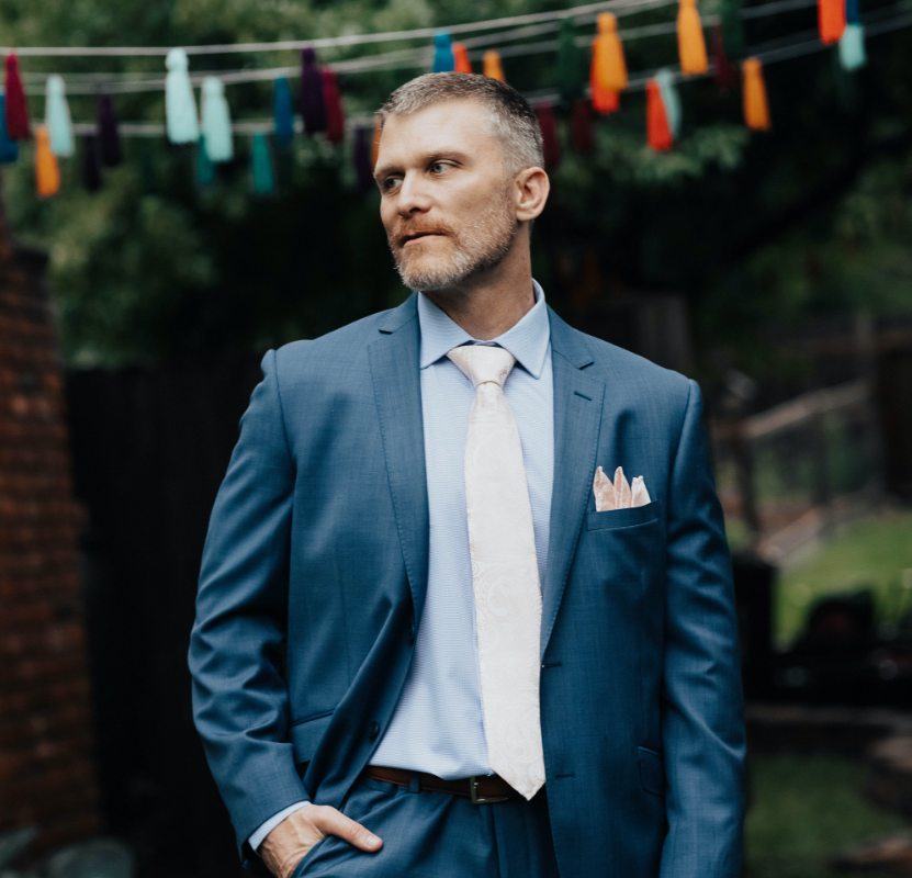 A man in a suit and tie is standing in front of a string of lights.