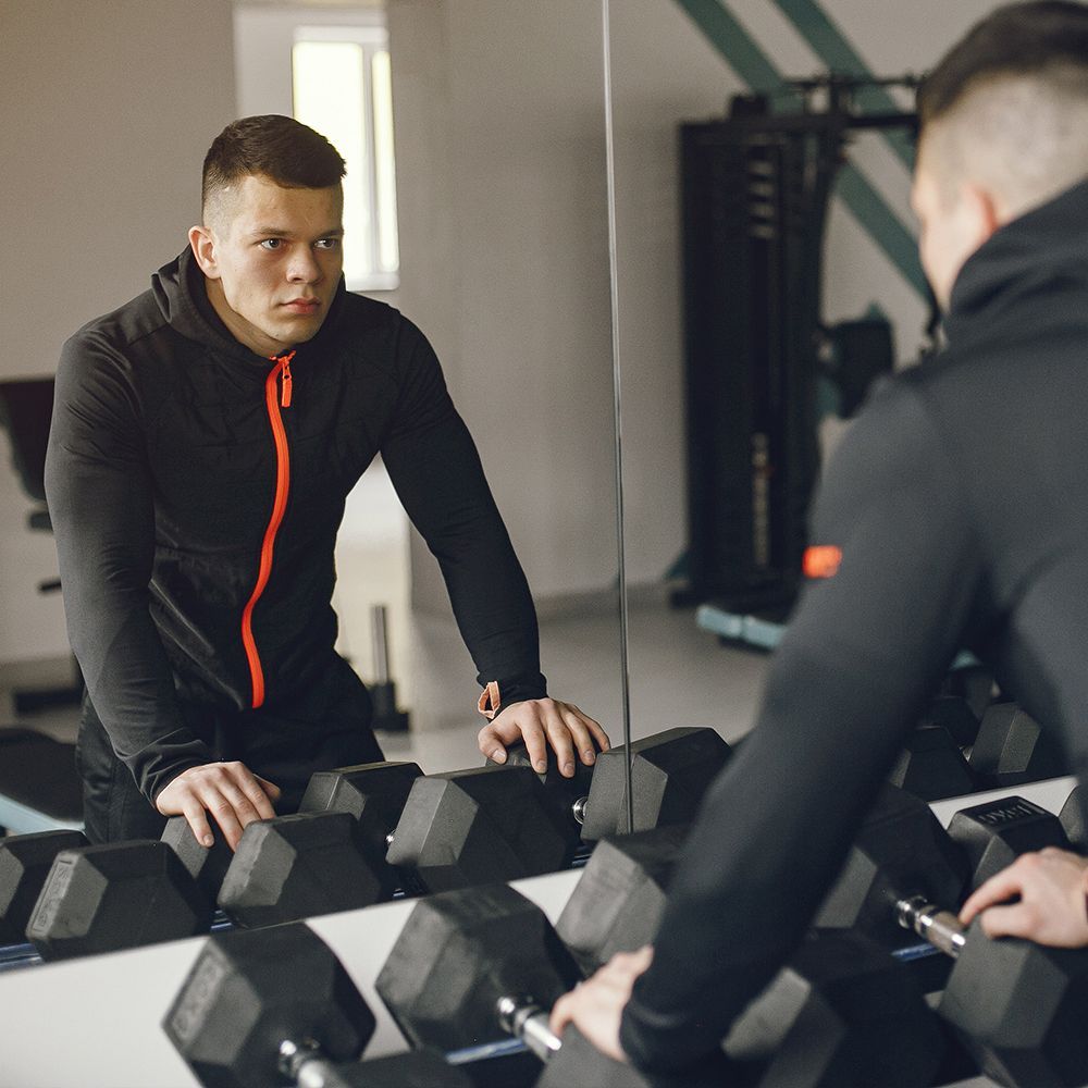 A man is looking at himself in the mirror in a gym.