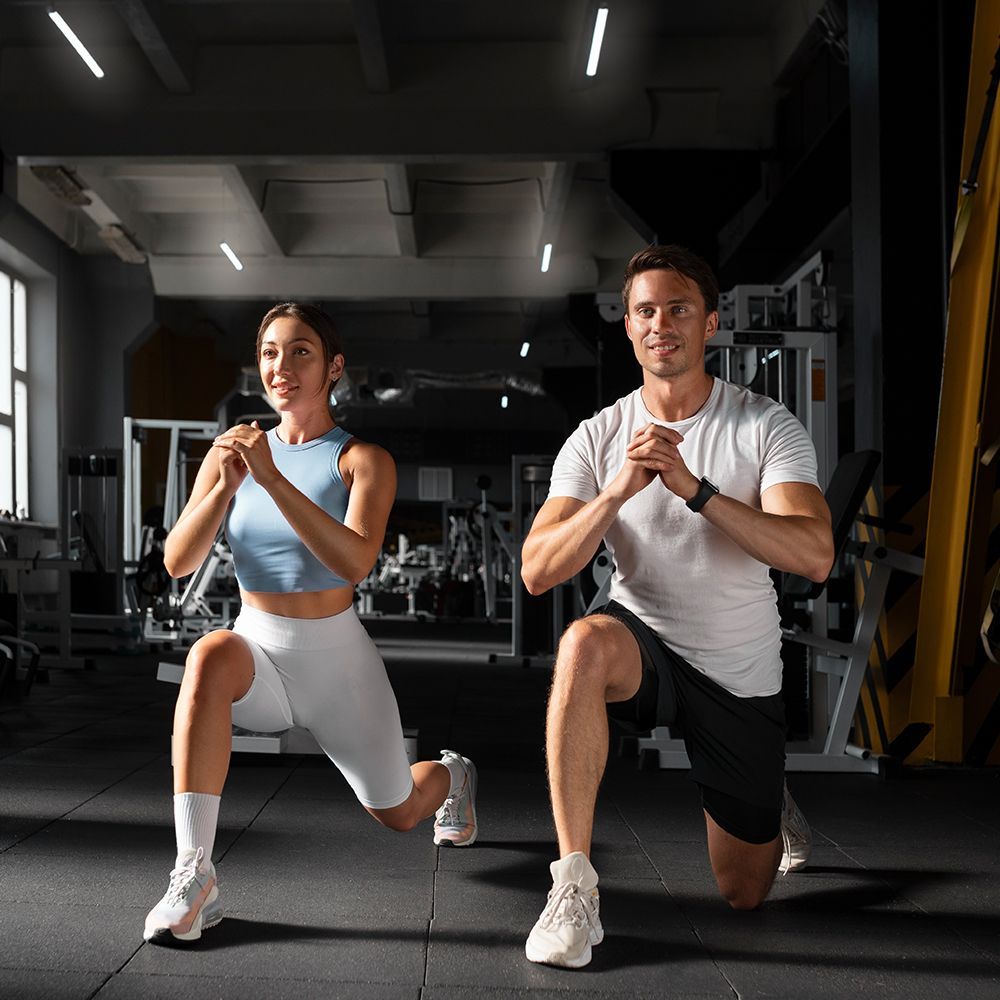 A man and a woman are doing lunges in a gym.