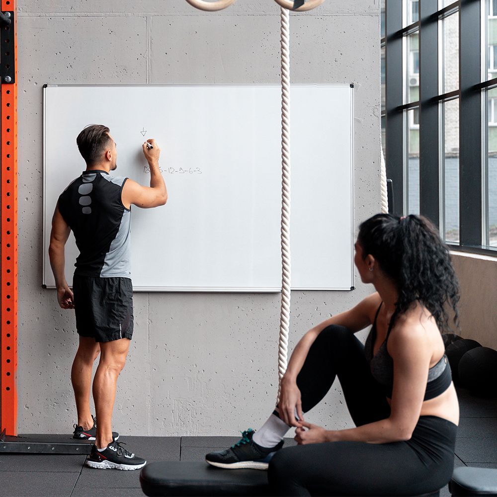 A woman is sitting on a yoga mat holding a dumbbell in front of a laptop.