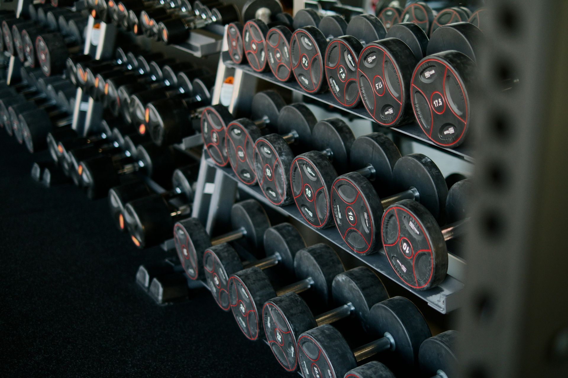 Weights rack at a gym with rows of dumbbells and weight plates.
