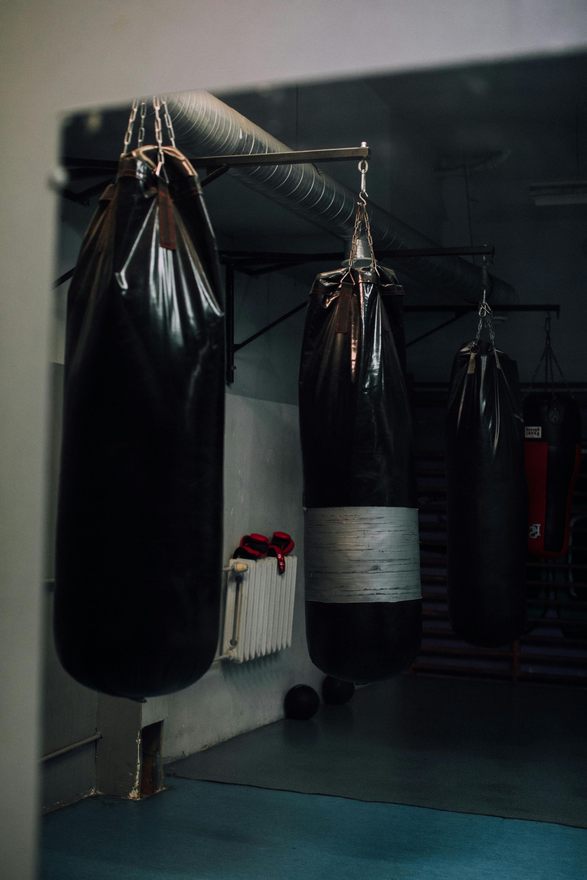 Boxing gym with three hanging heavy bags, dark interior, blue floor.