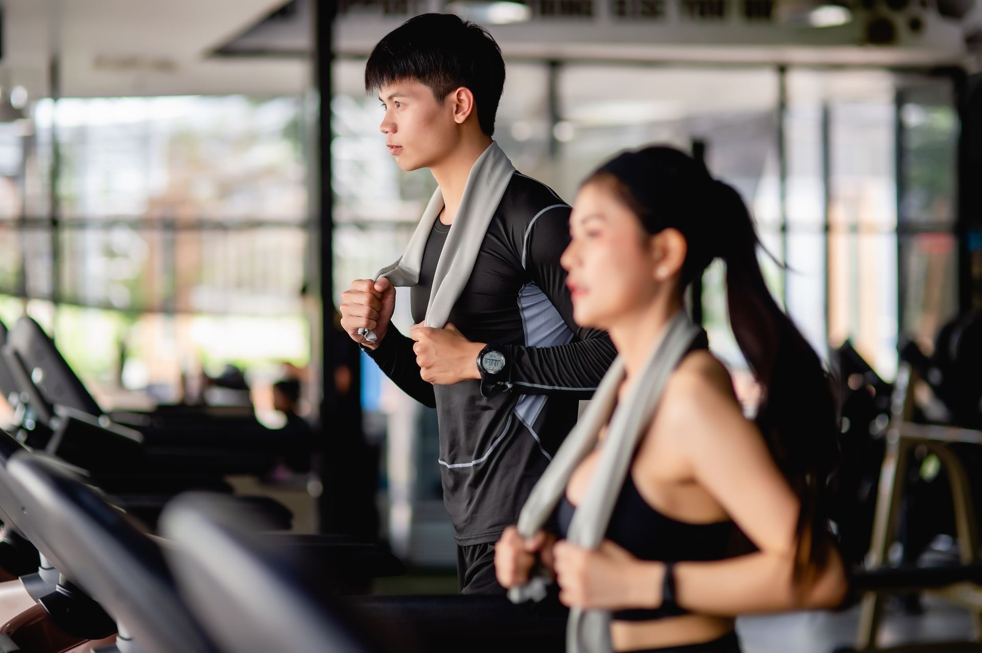 A man and a woman are running on treadmills in a gym.