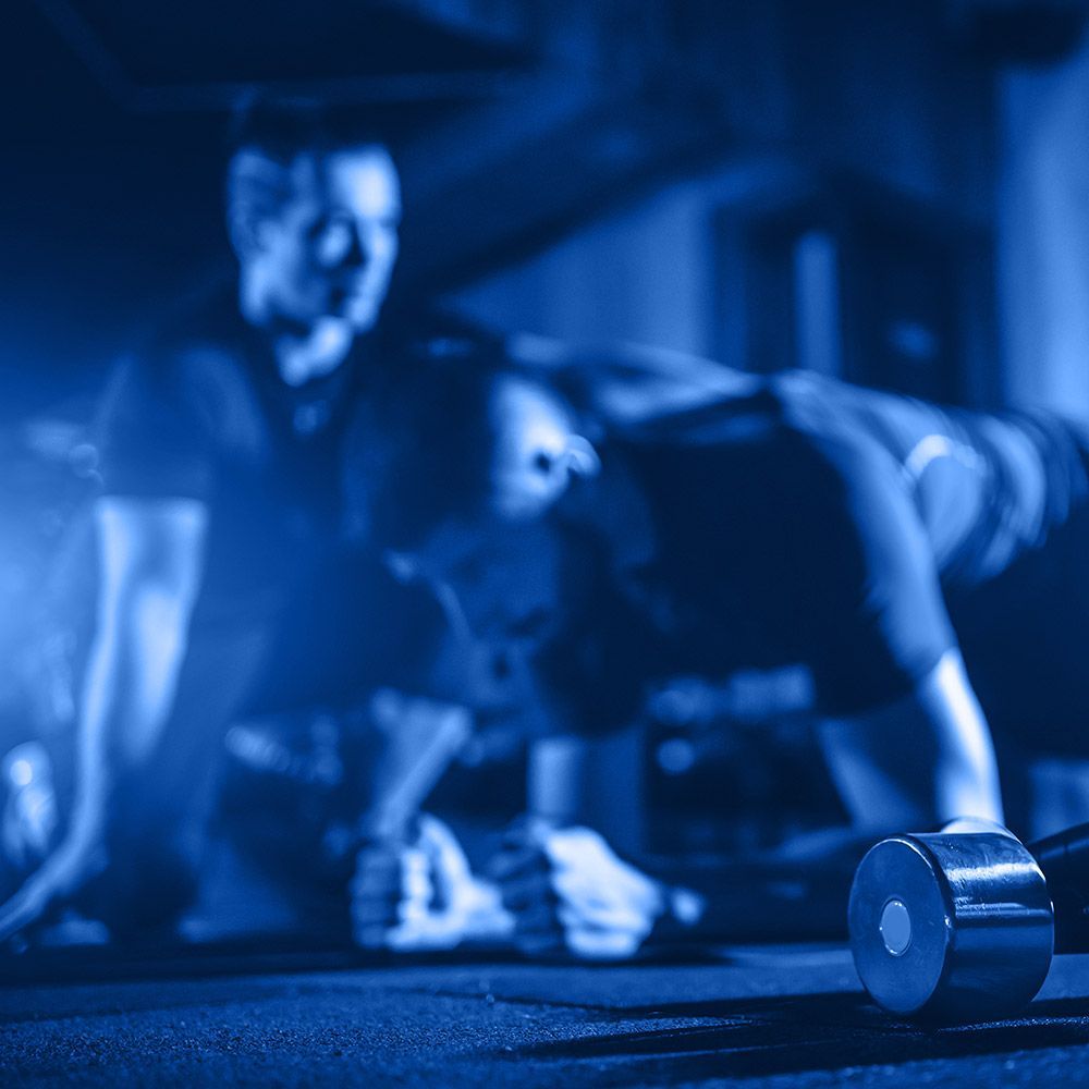 A man and a woman are doing push ups in a gym.