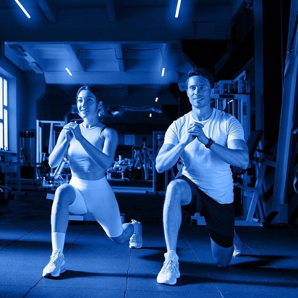 A man and a woman are doing lunges in a gym