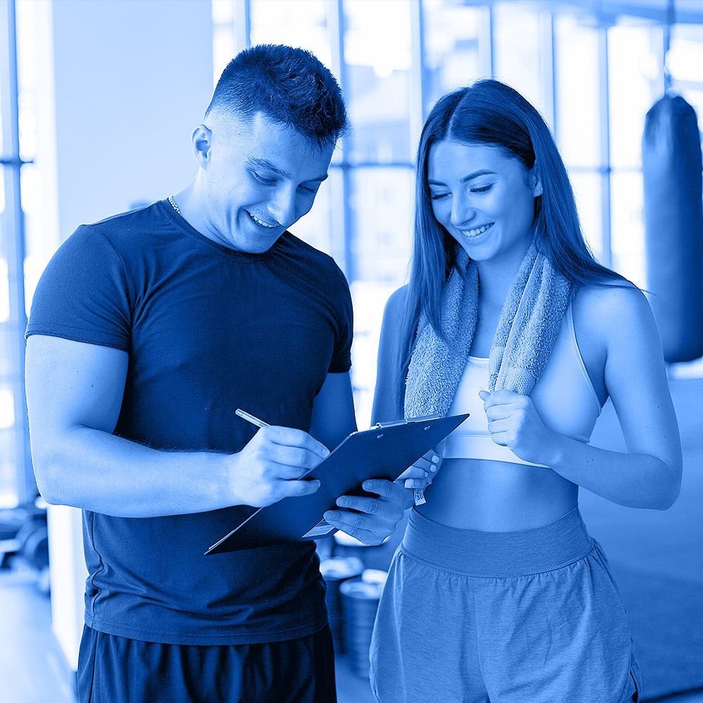 A man and a woman are looking at a clipboard in a gym.