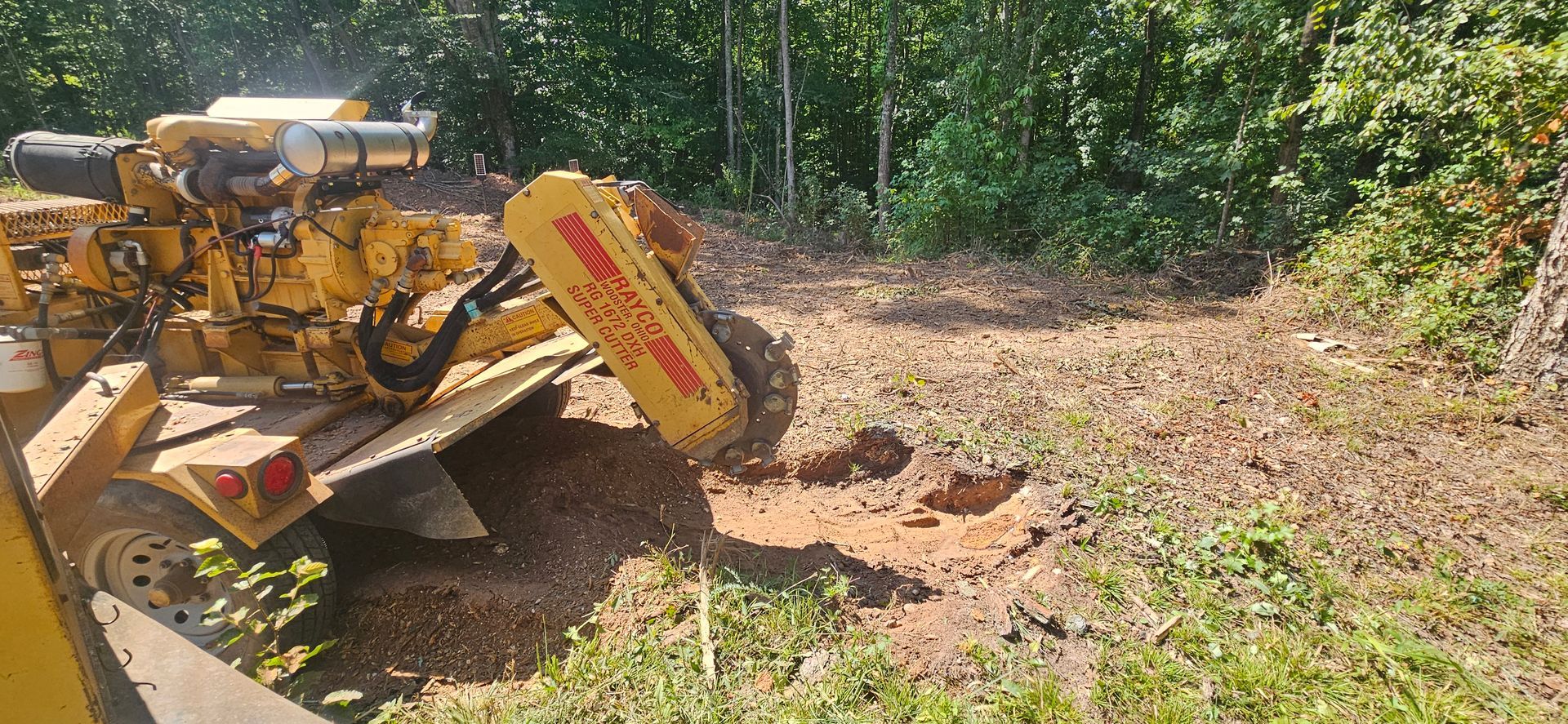 A yellow stump grinder is cutting a tree stump in the grass.