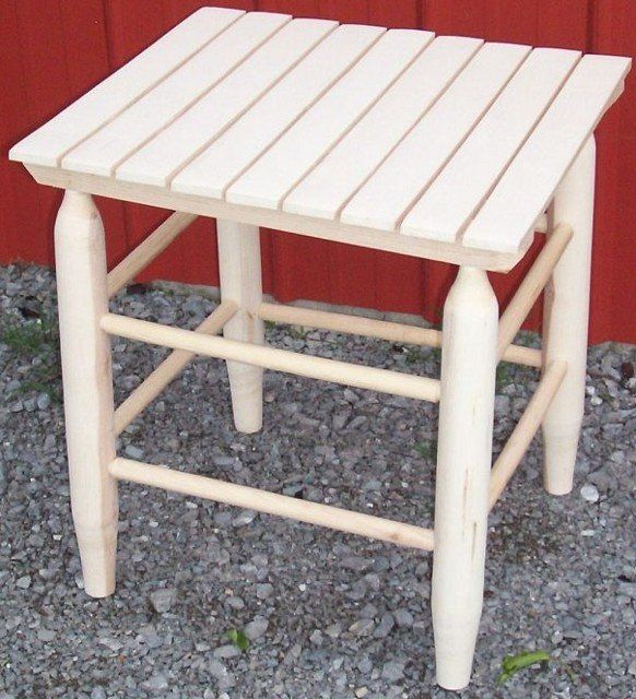 A small wooden stool sits on gravel in front of a red wall