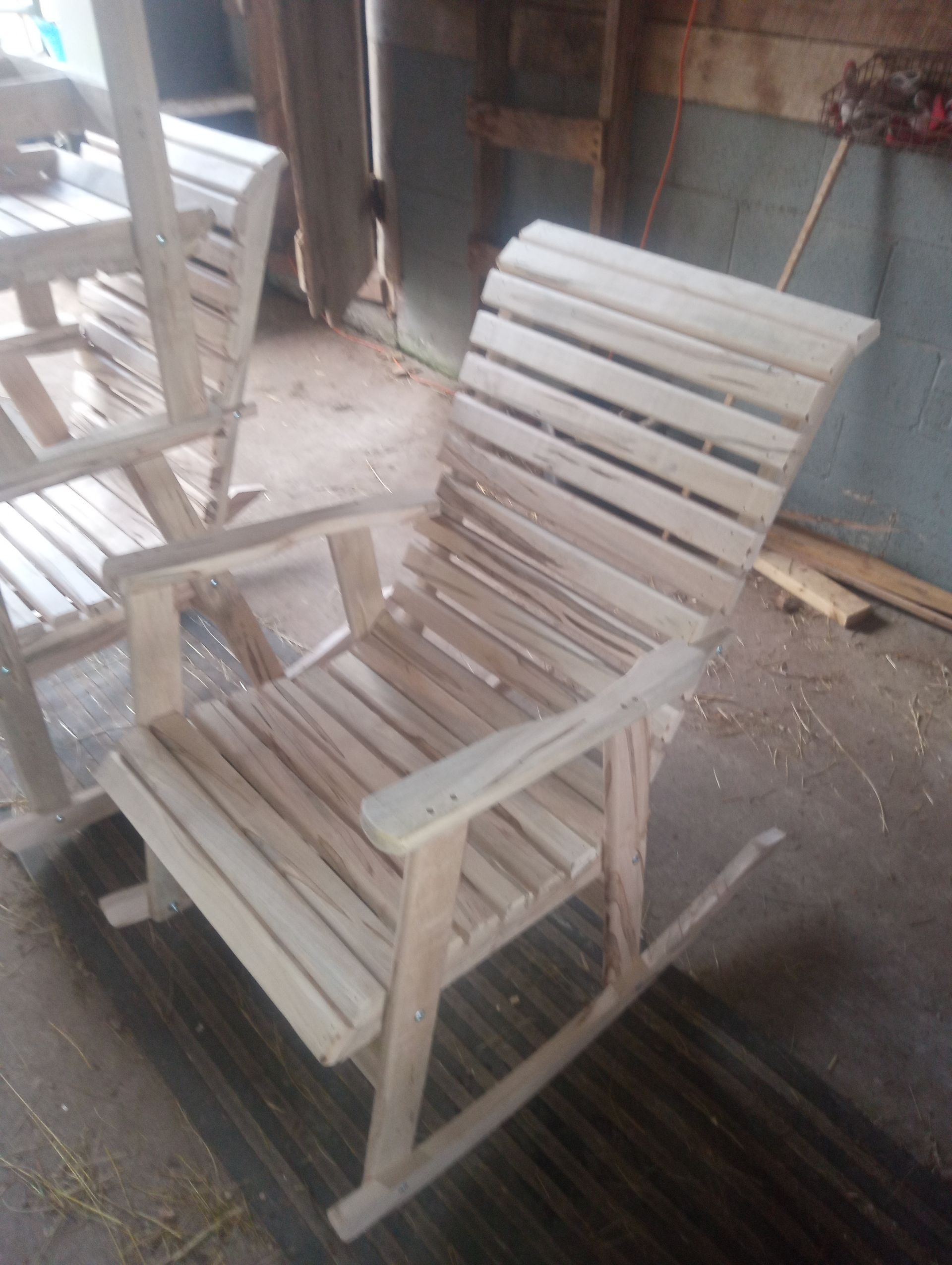A wooden rocking chair sits in front of a pile of wooden chairs