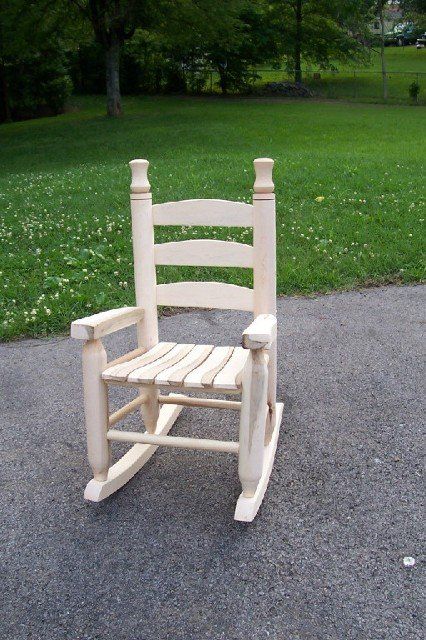 A wooden rocking chair is sitting on the side of a road.