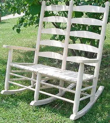 A white rocking chair is sitting on top of a lush green field.