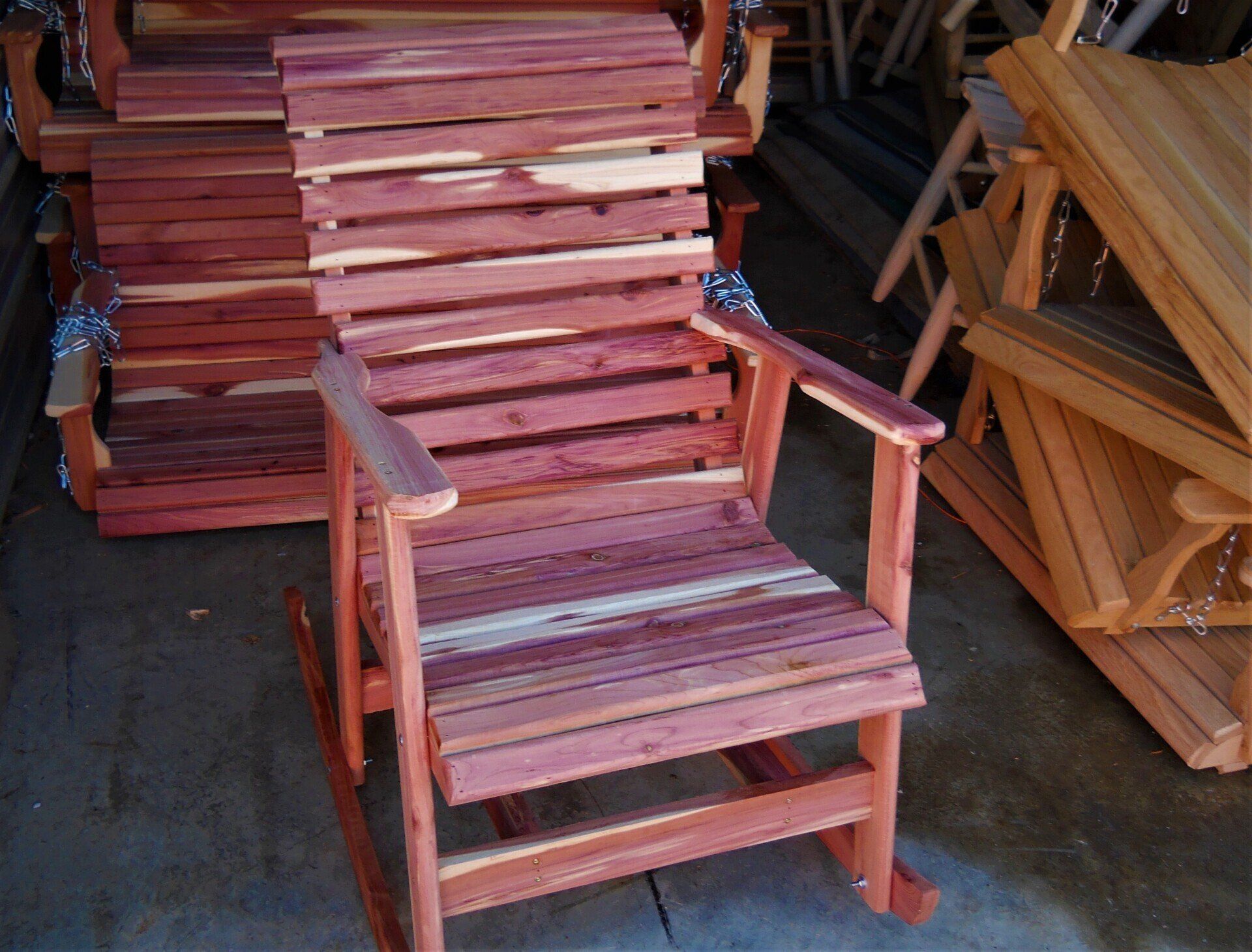 A wooden rocking chair sits in front of a pile of wooden chairs