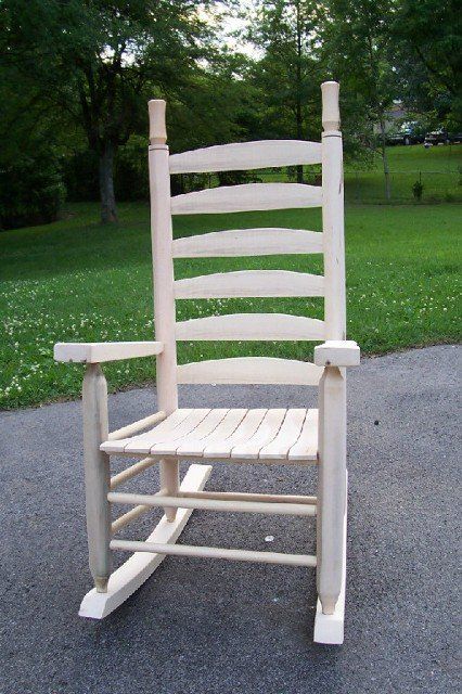 A white wooden rocking chair is sitting on the side of a road