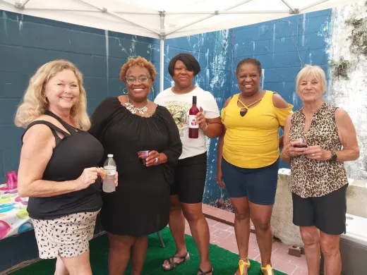 Five people posing under a white canopy, holding drinks at an outdoor gathering