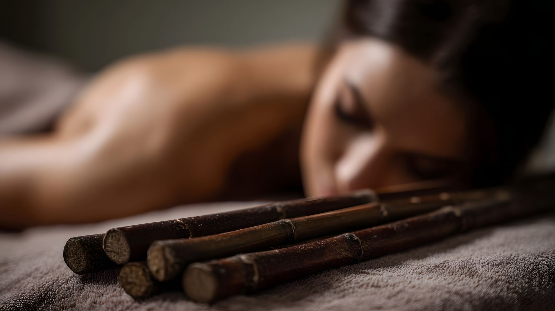 Woman lying face down beside three wooden massage sticks on a towel