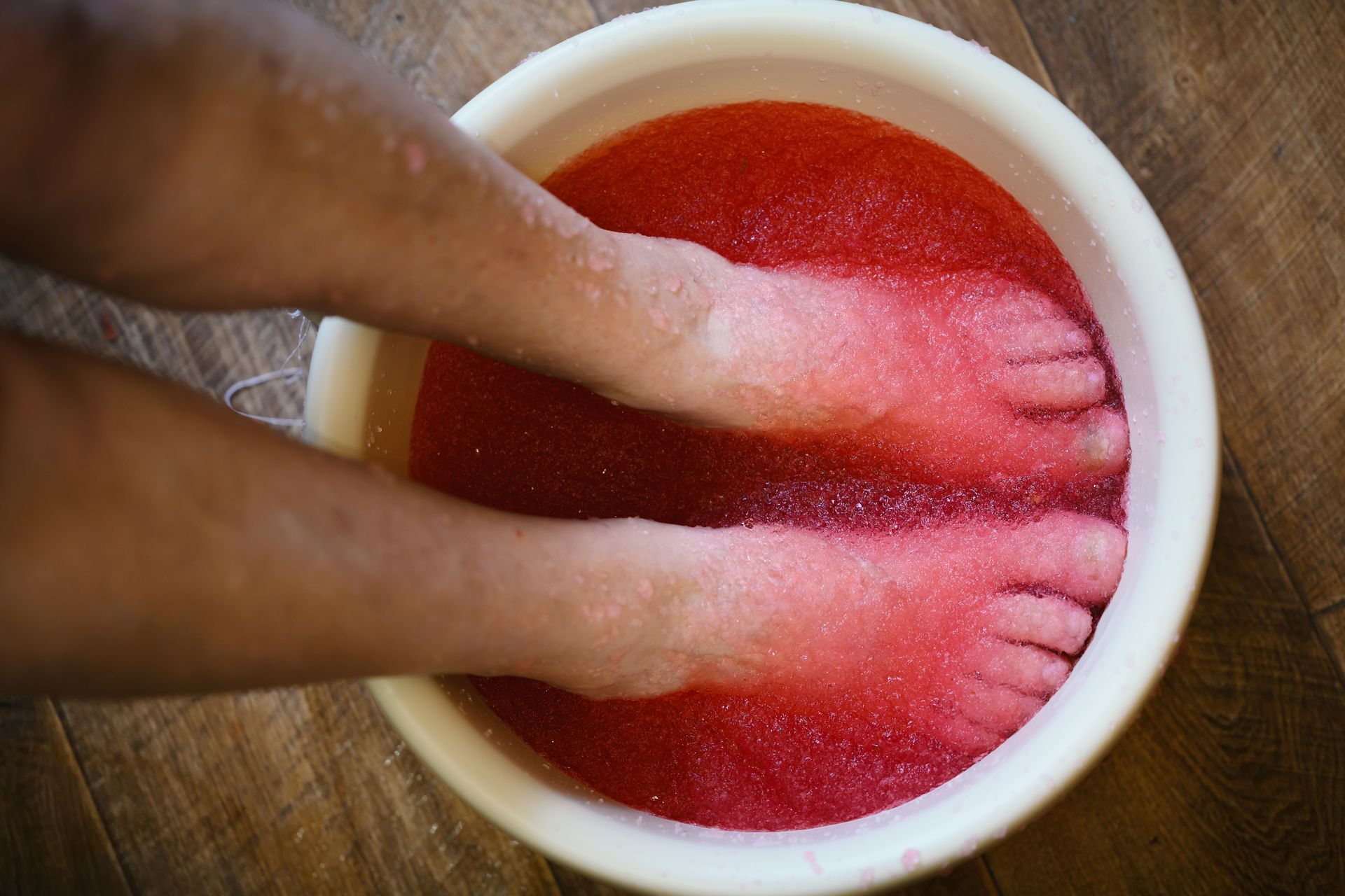 Hands soaking in a white bowl of red liquid