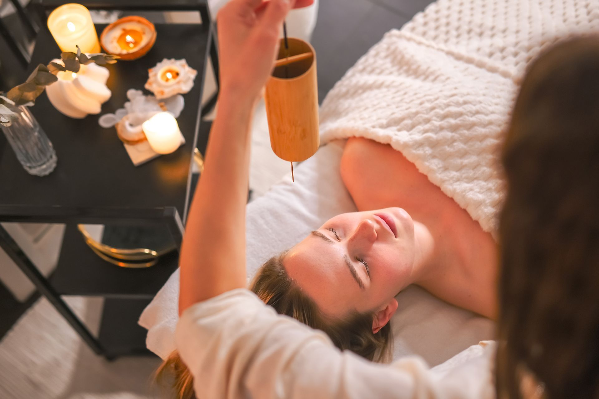 Person relaxing on a massage table while another uses a facial roller in a warm spa setting