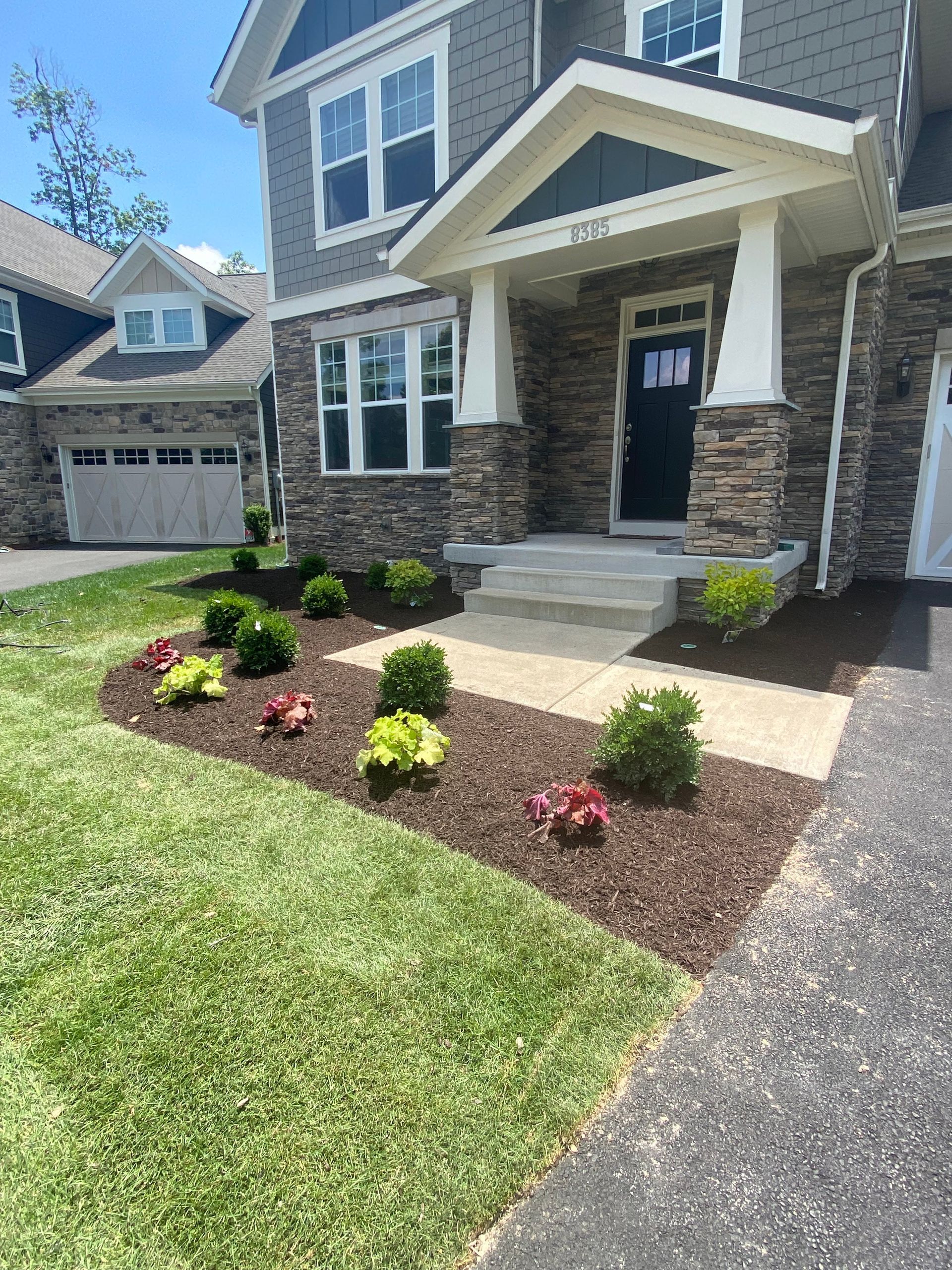 The front of a house with a lush green lawn and flowers in front of it.