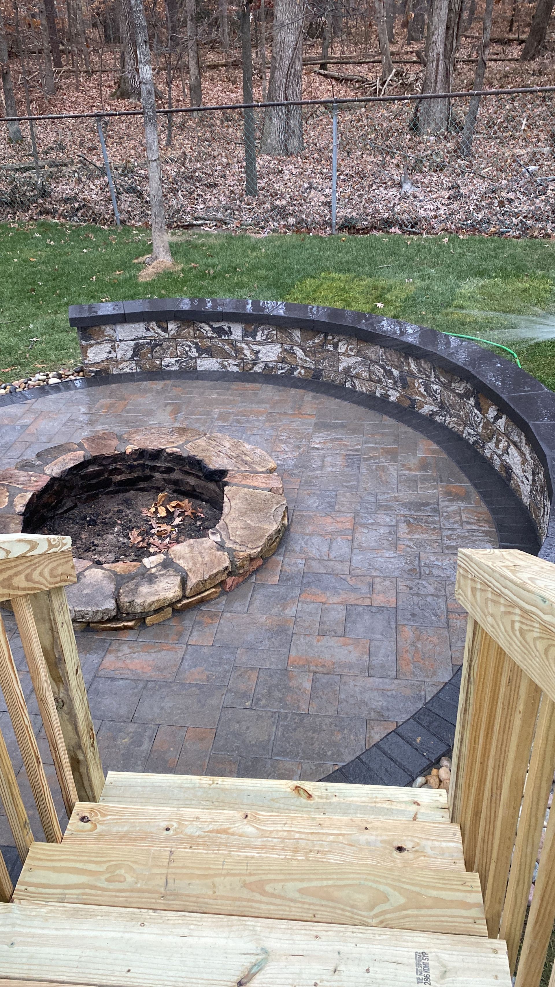 A fire pit is surrounded by a stone wall and stairs in a backyard.