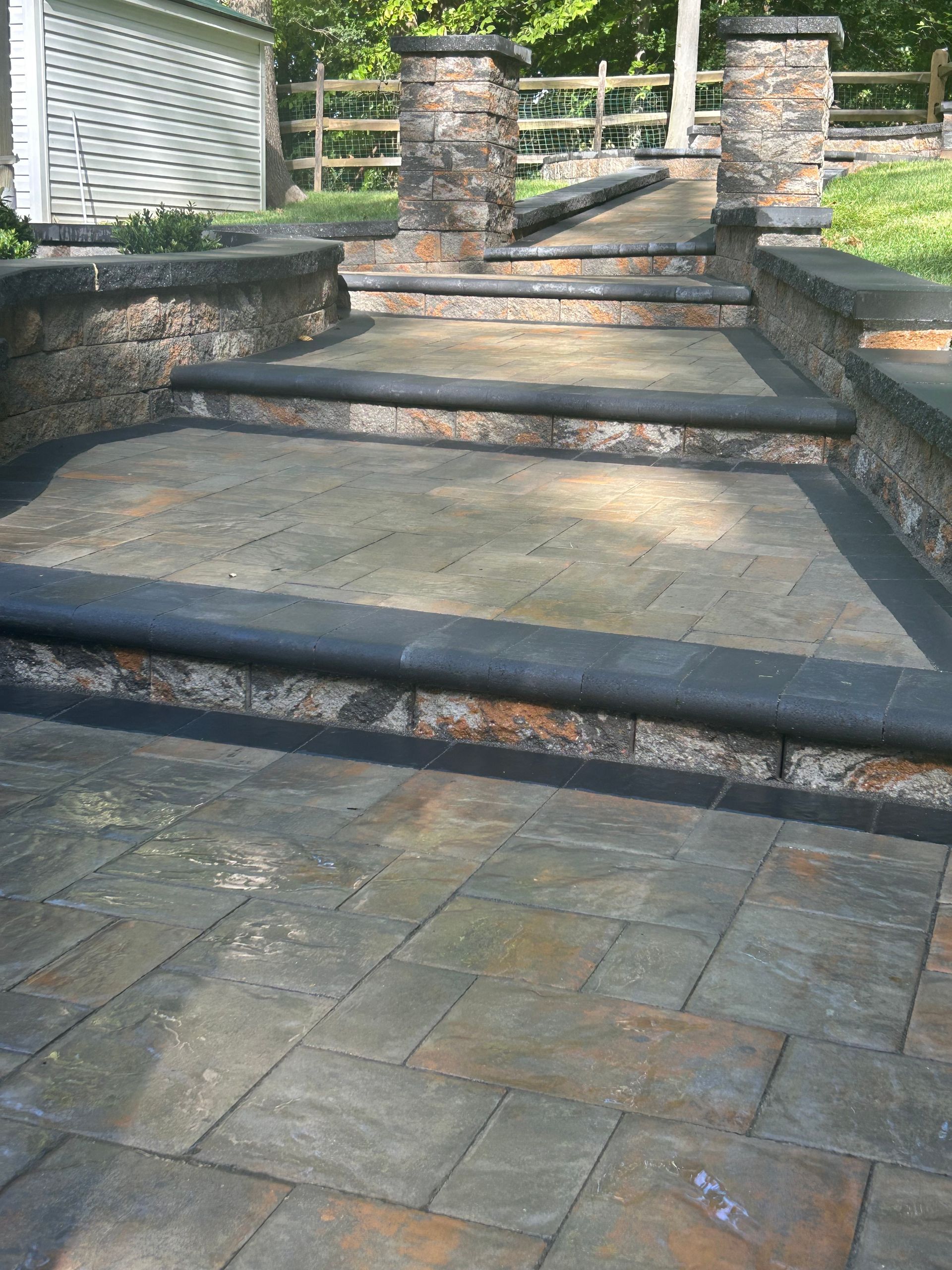 A stone walkway with stairs and a fence in the background