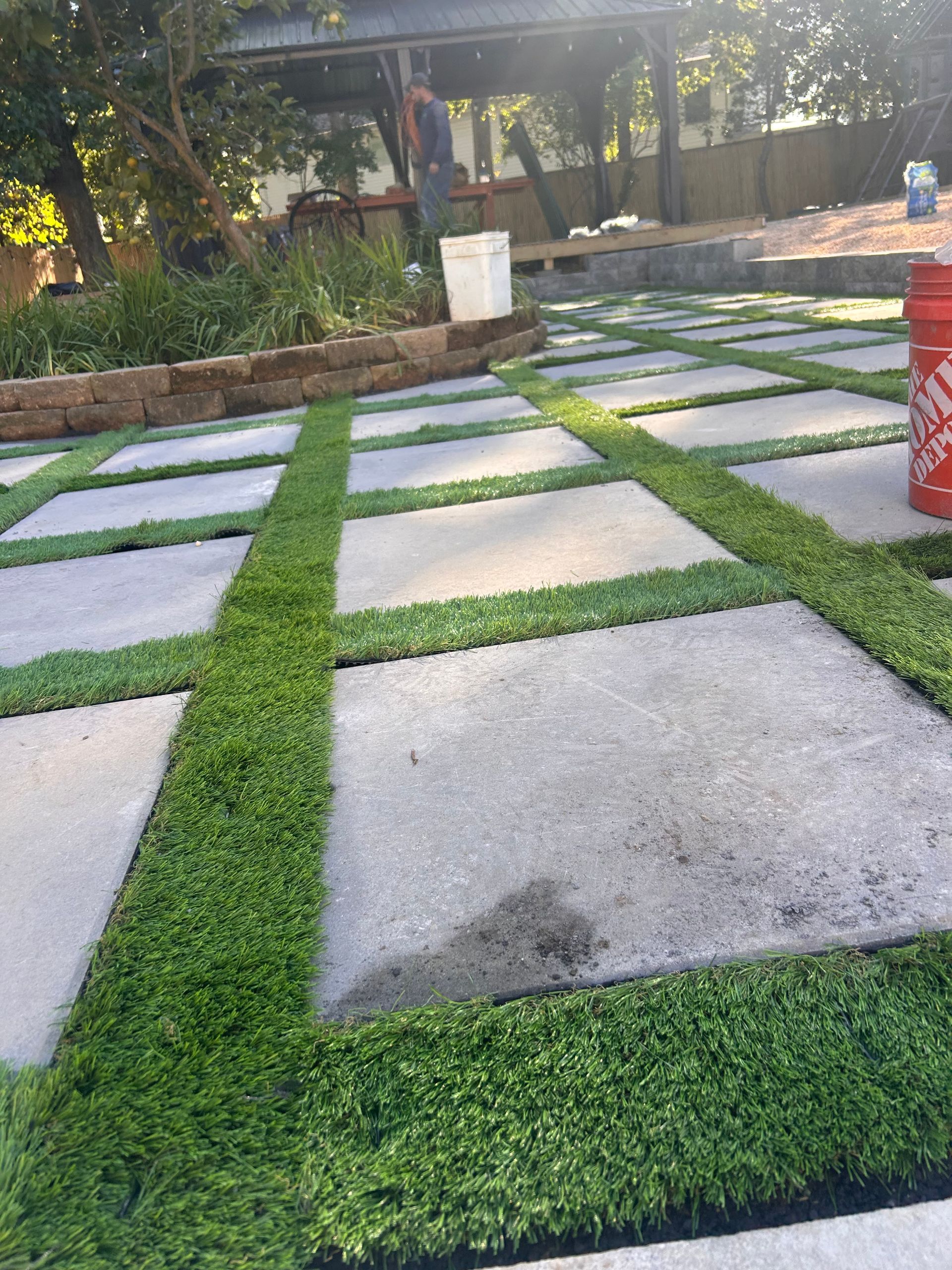 A red bucket is sitting on the ground next to a lawn.