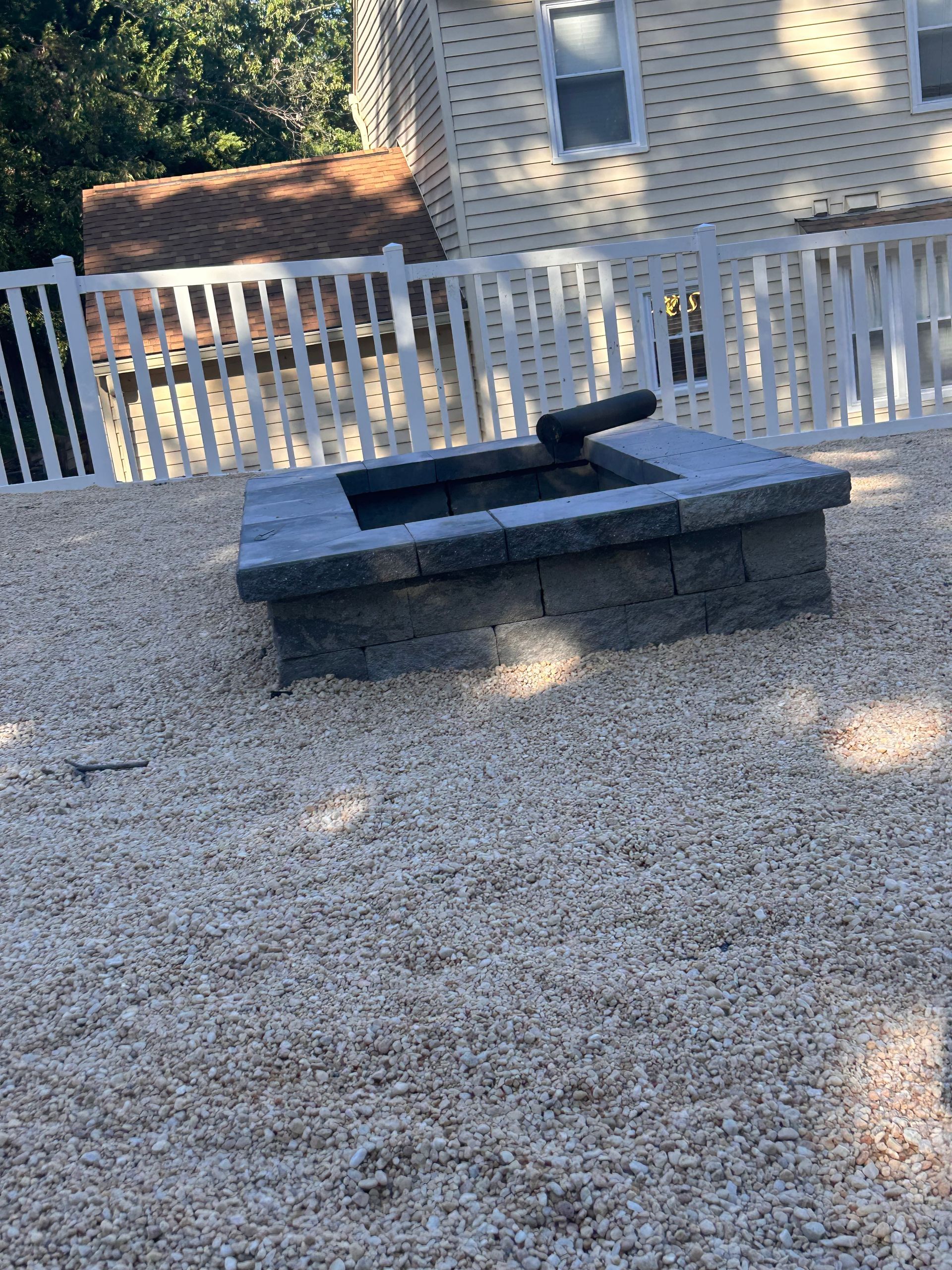 A fire pit is sitting in the gravel in front of a house.