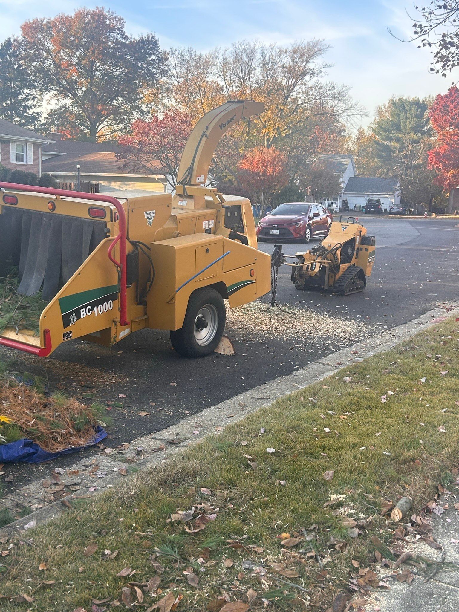 A tree chipper is sitting on the side of the road next to a stump grinder.