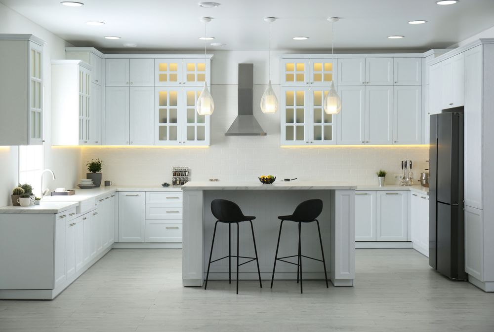 A modern kitchen with white cabinets , stools , a refrigerator and a sink.