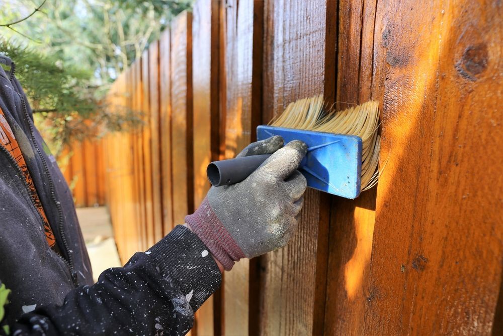 A person is painting a wooden fence with a brush.