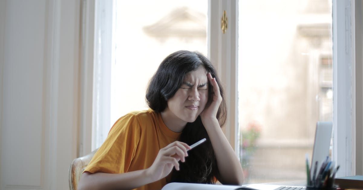 A woman is sitting at a desk with a laptop and a thermometer in her hand.