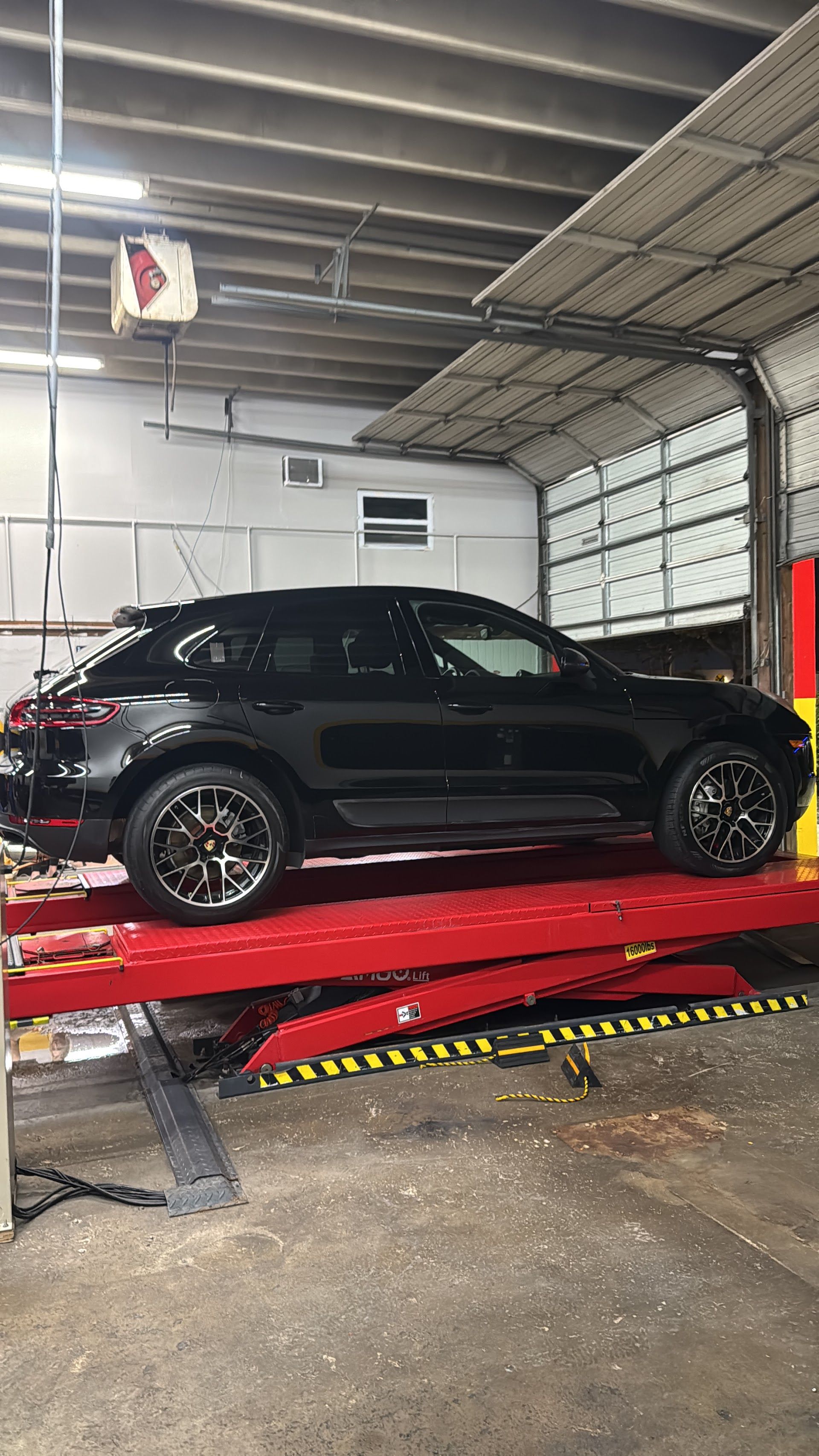 Black Porsche SUV on a red car lift inside a garage. | Jimmy's German Auto Repair