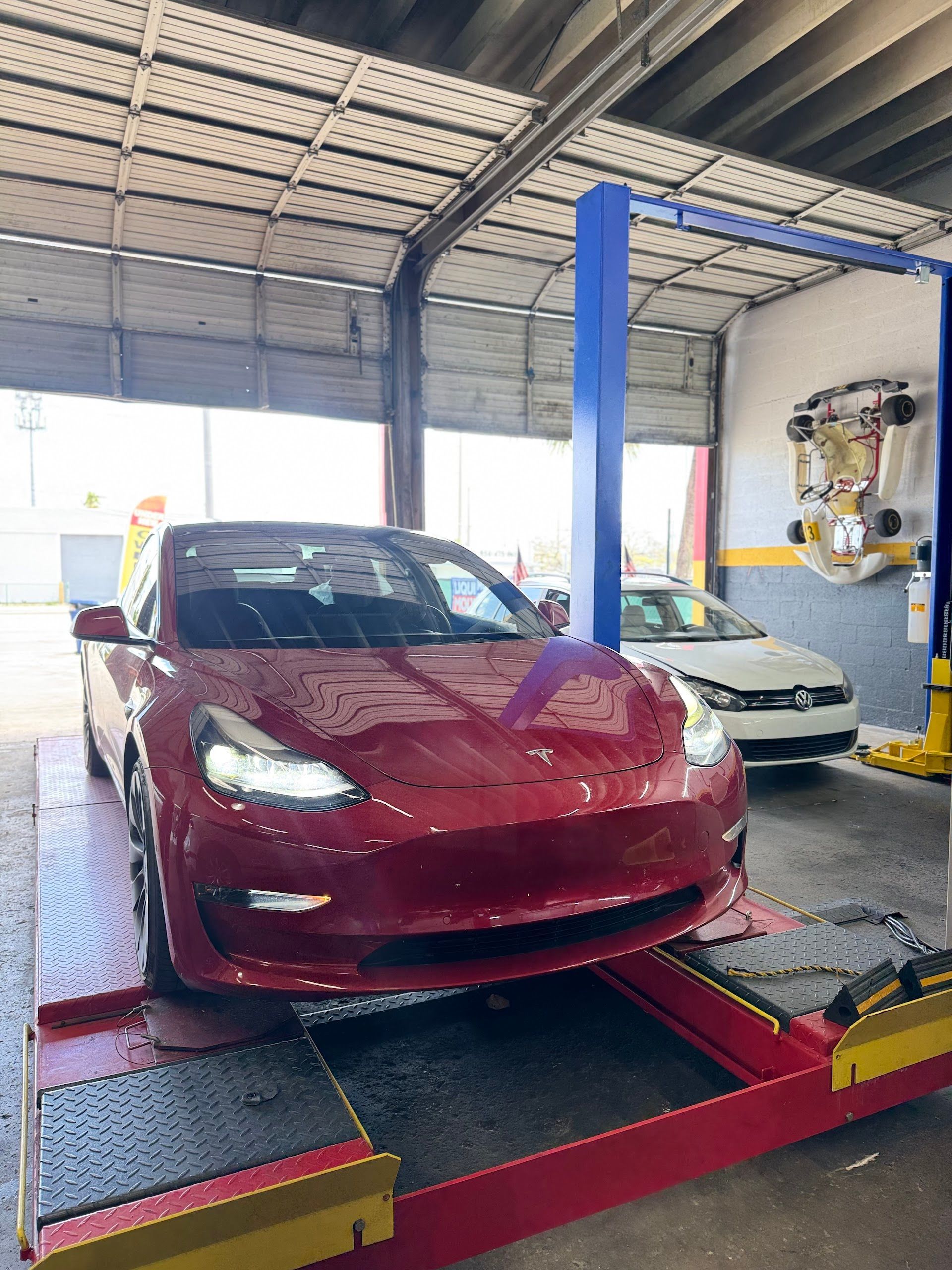 Red Tesla car on a lift in a garage, another car in the background. | Jimmy's German Auto Repair