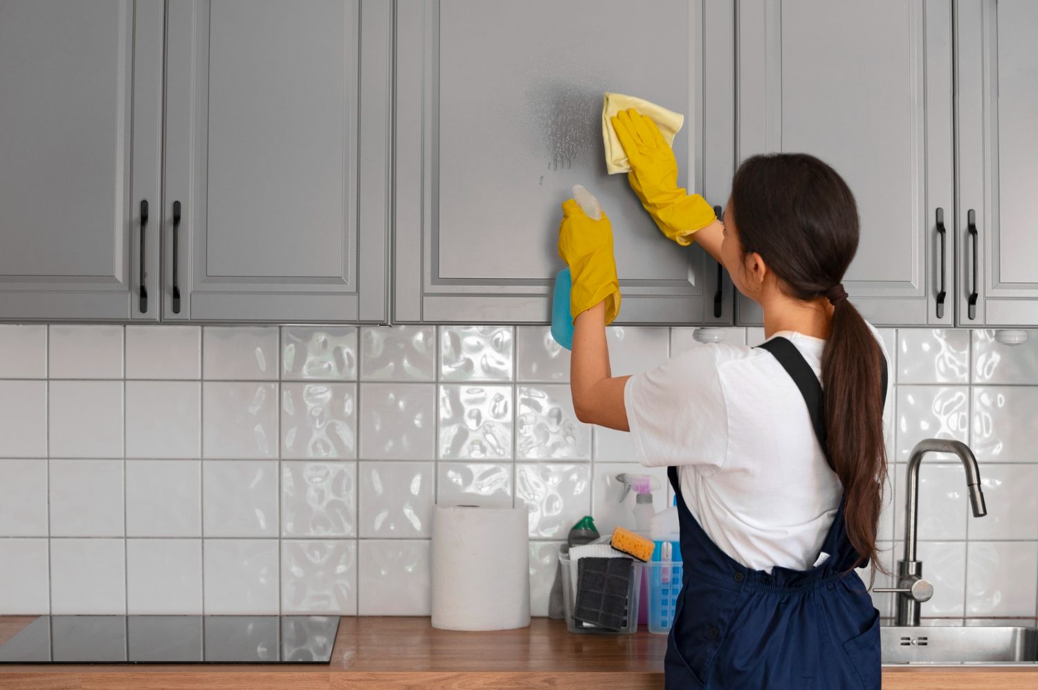 A woman is cleaning the cabinets in a kitchen.