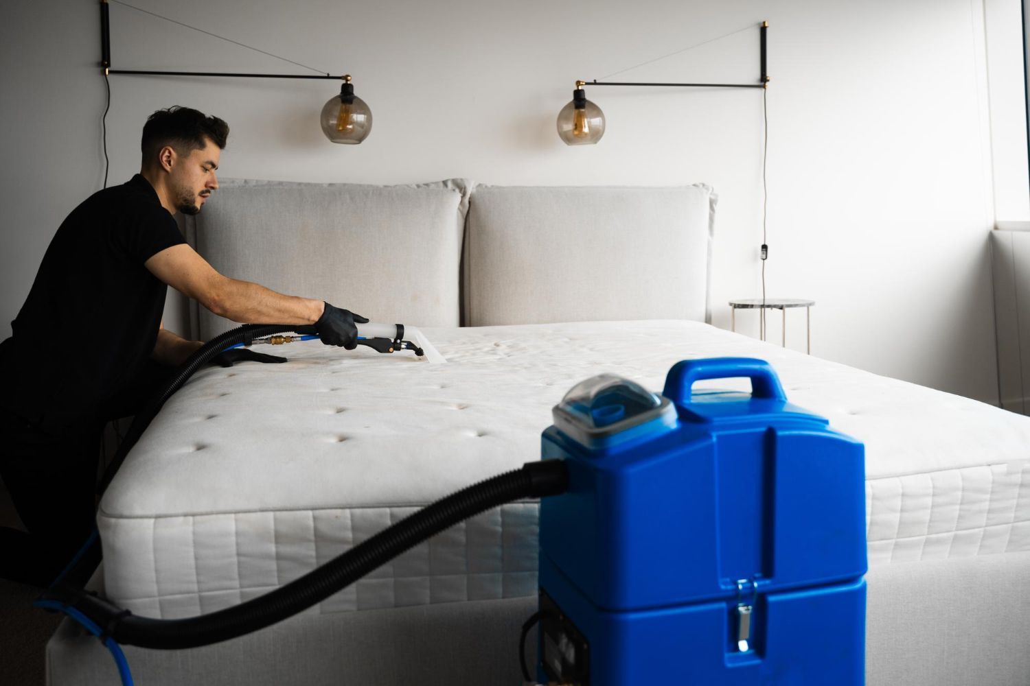 A man is cleaning a mattress with a vacuum cleaner.