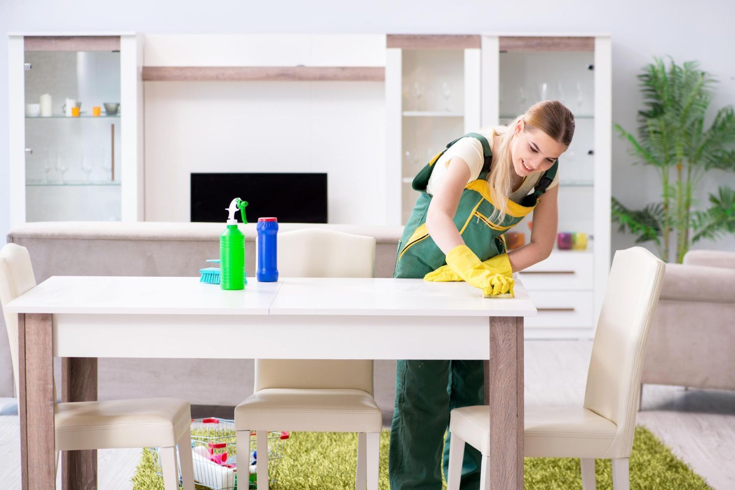 Woman in cleaning uniform wiping a white table in a living room.