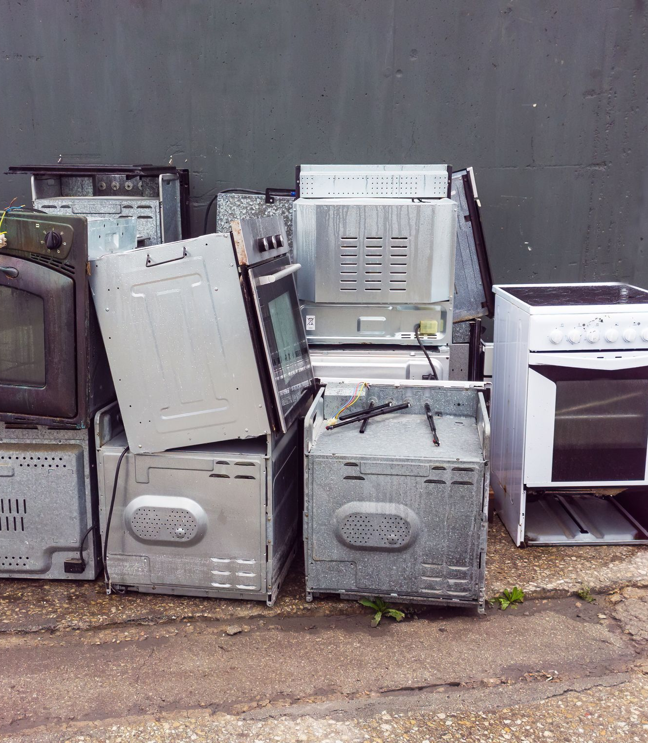 Pile of discarded ovens and stoves against a gray wall.