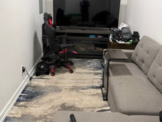 Cluttered living room with a gray sofa, gaming chair, TV stand, and rug on the floor