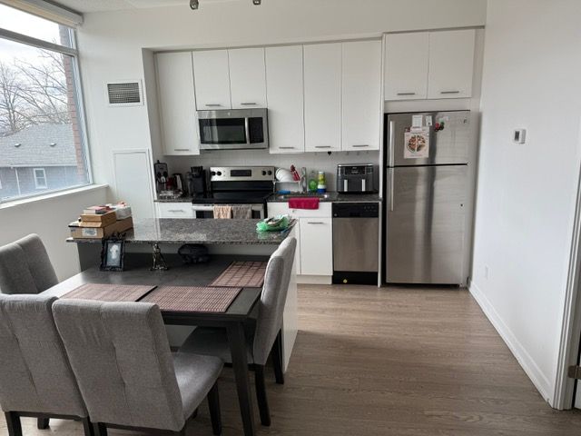 Modern kitchen and dining area with gray chairs, white cabinets, stainless steel appliances, and large window.