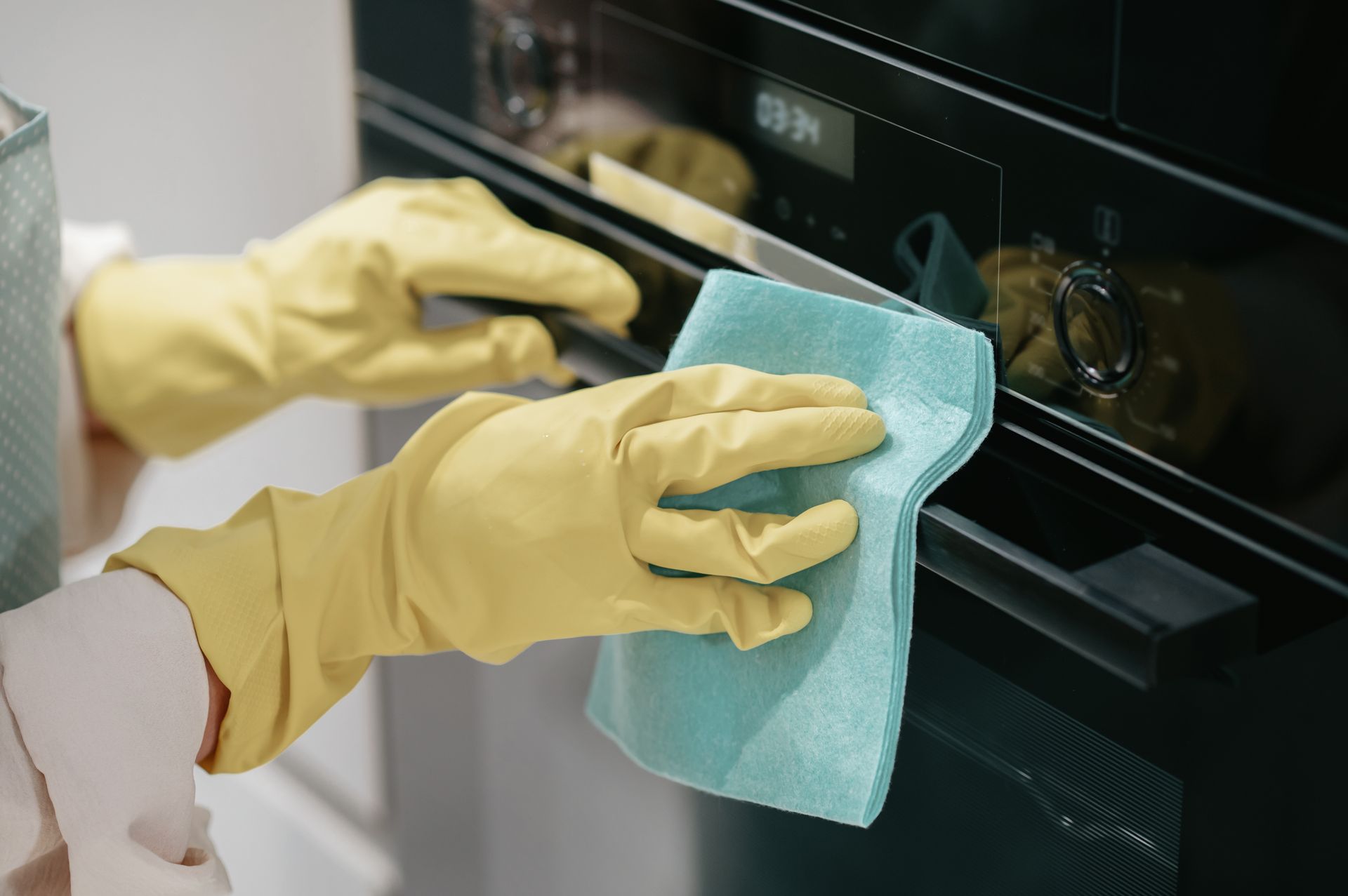 A person wearing yellow gloves is cleaning an oven with a cloth.